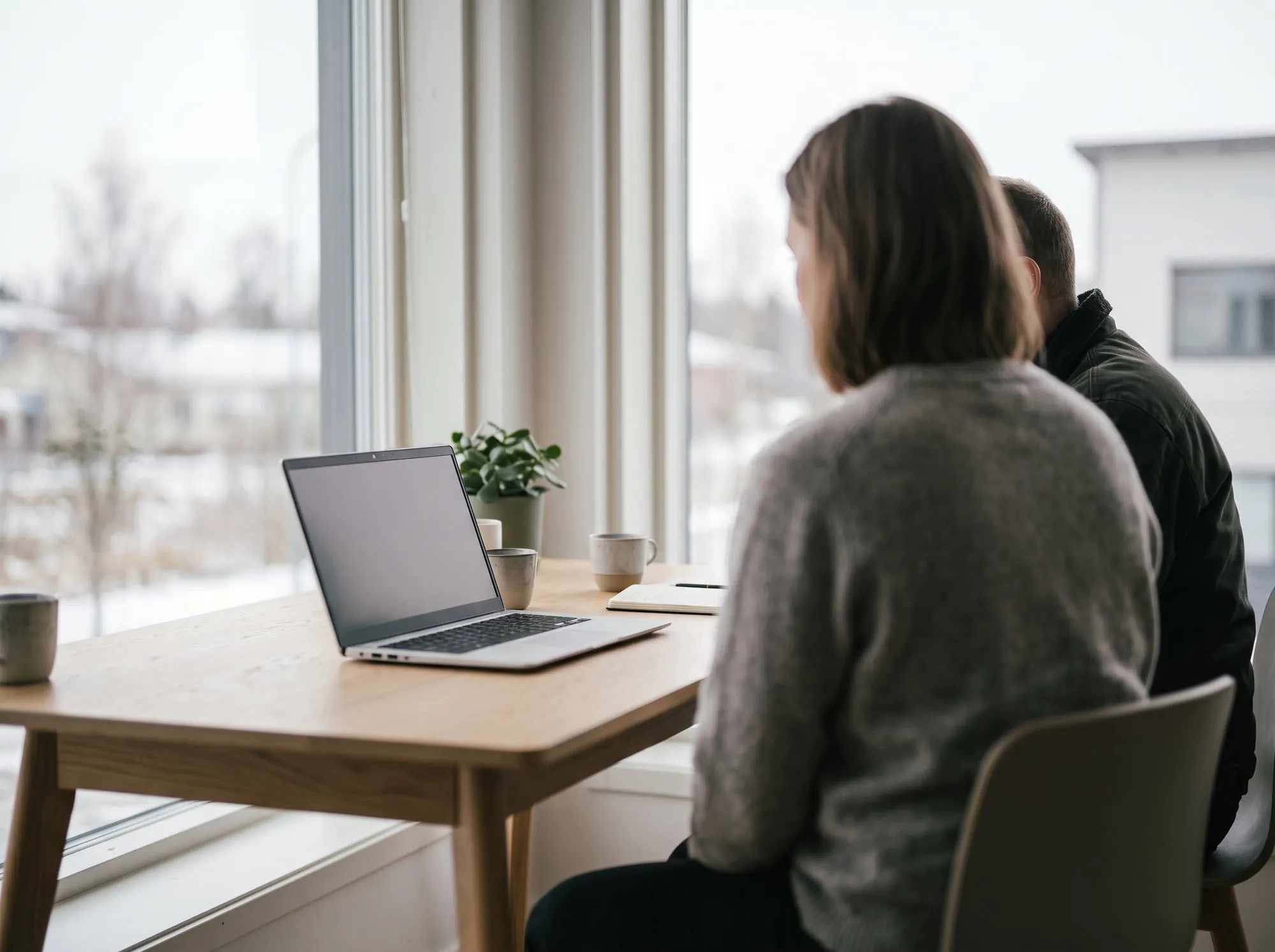 Two people at a laptop in a bright office, seen from behind