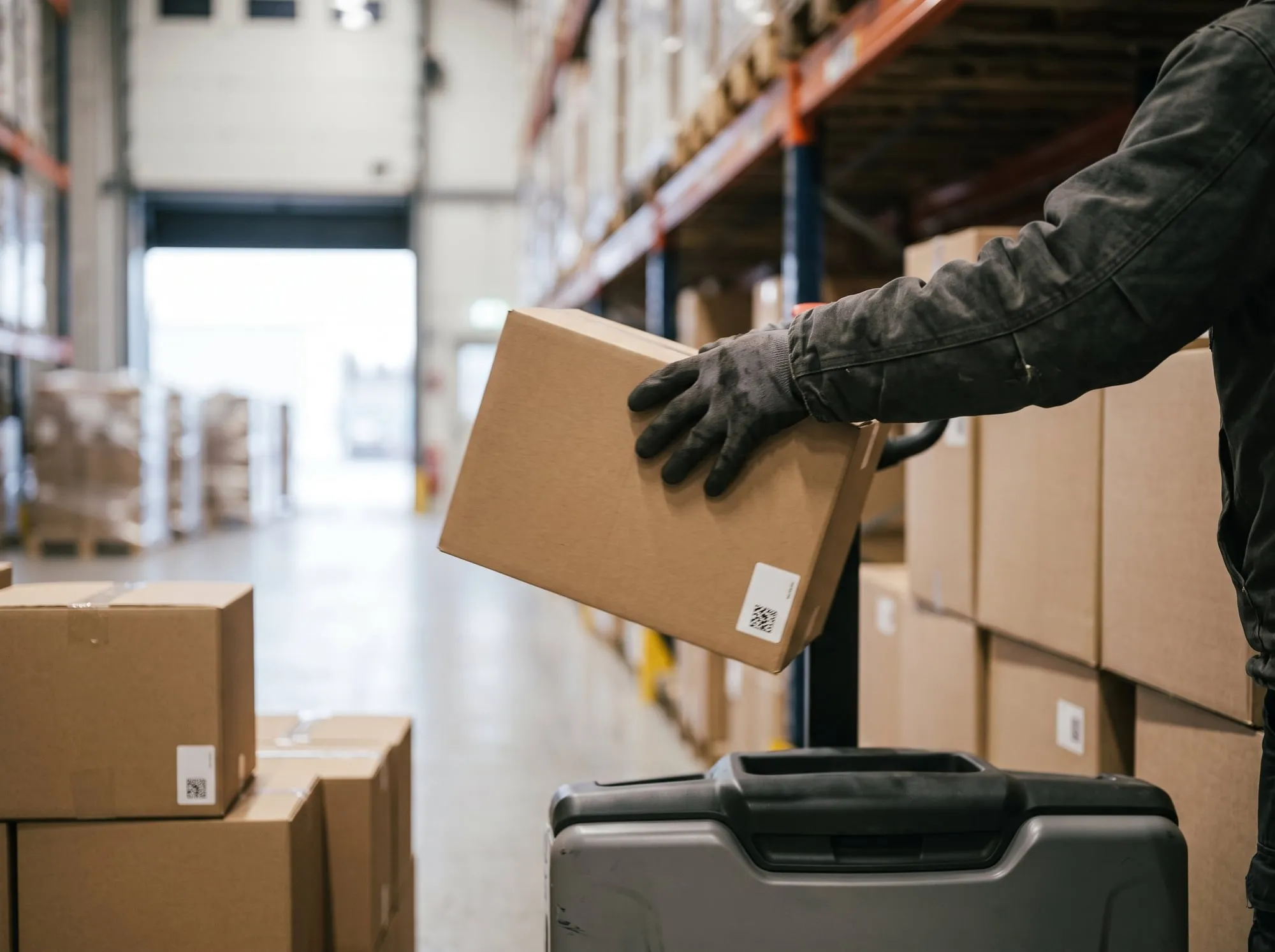 A gloved hand picking a carton from the shelf onto a pallet truck