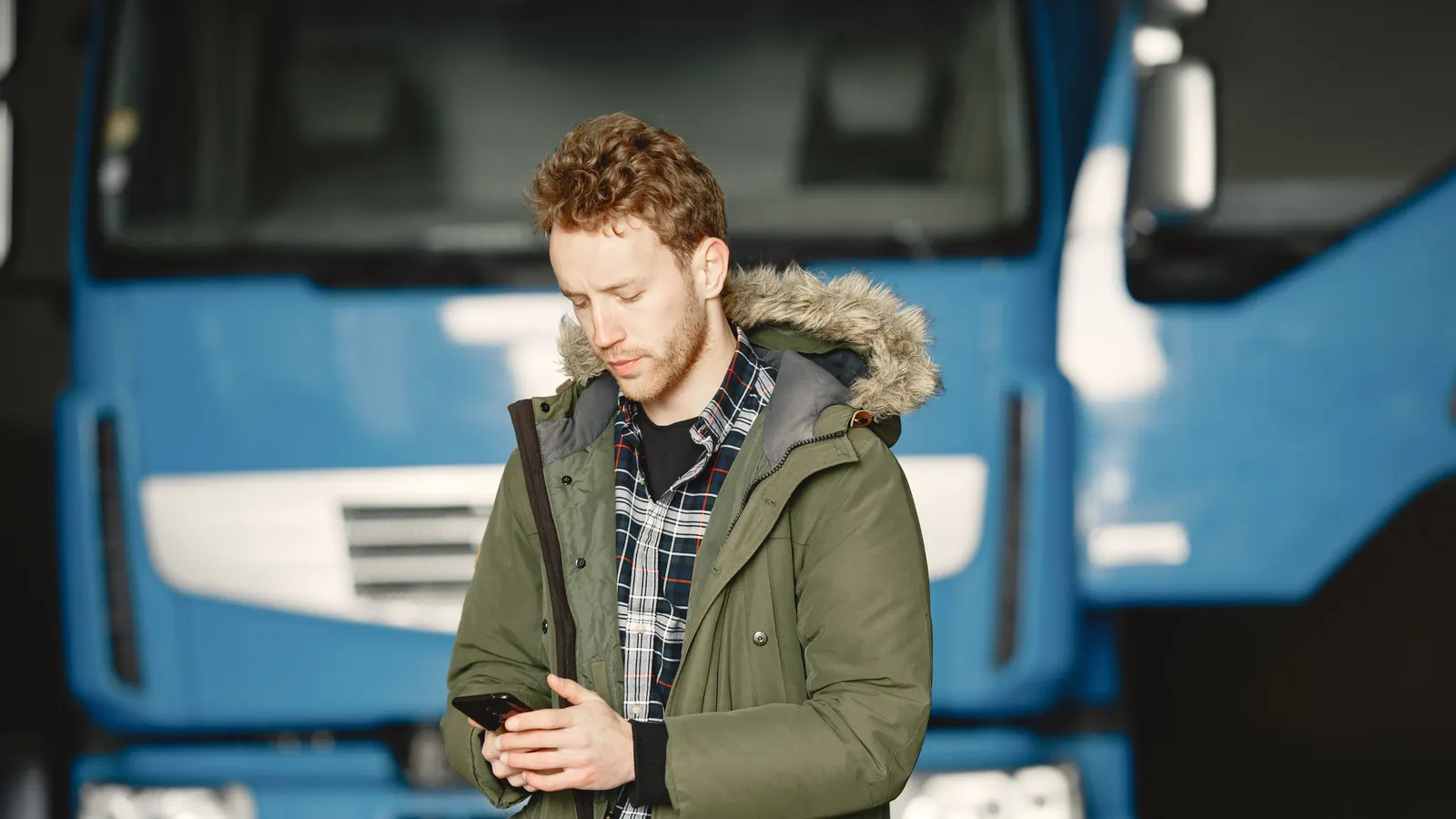 Ein Fahrer schaut auf sein Handy vor einer blauen europäischen Lkw-Kabine