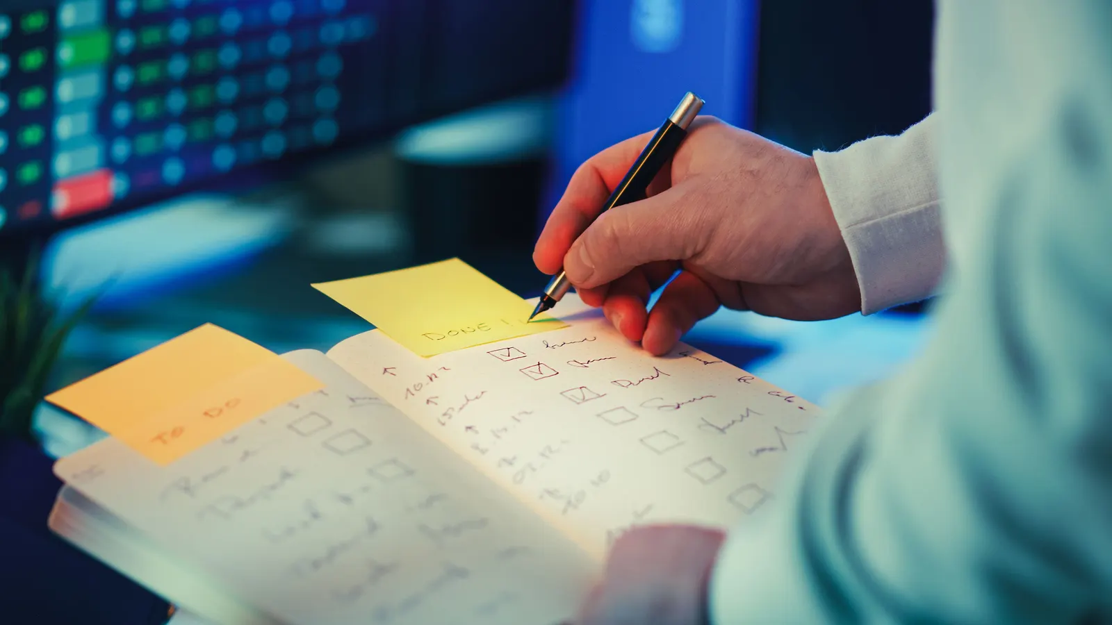 A hand ticking items off a handwritten checklist in a notebook on a desk