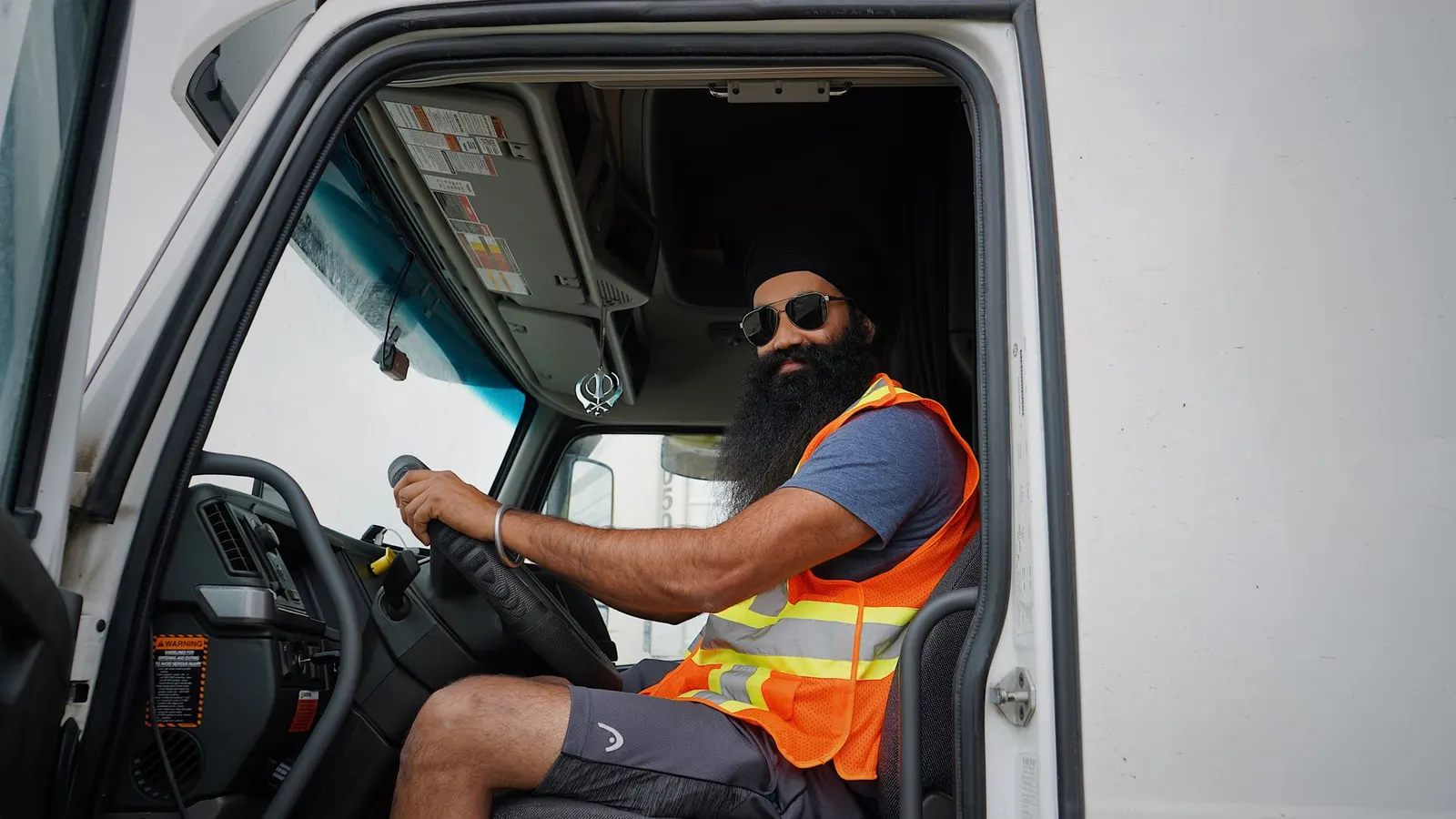 A truck driver in a high-visibility vest in the cab with the door open