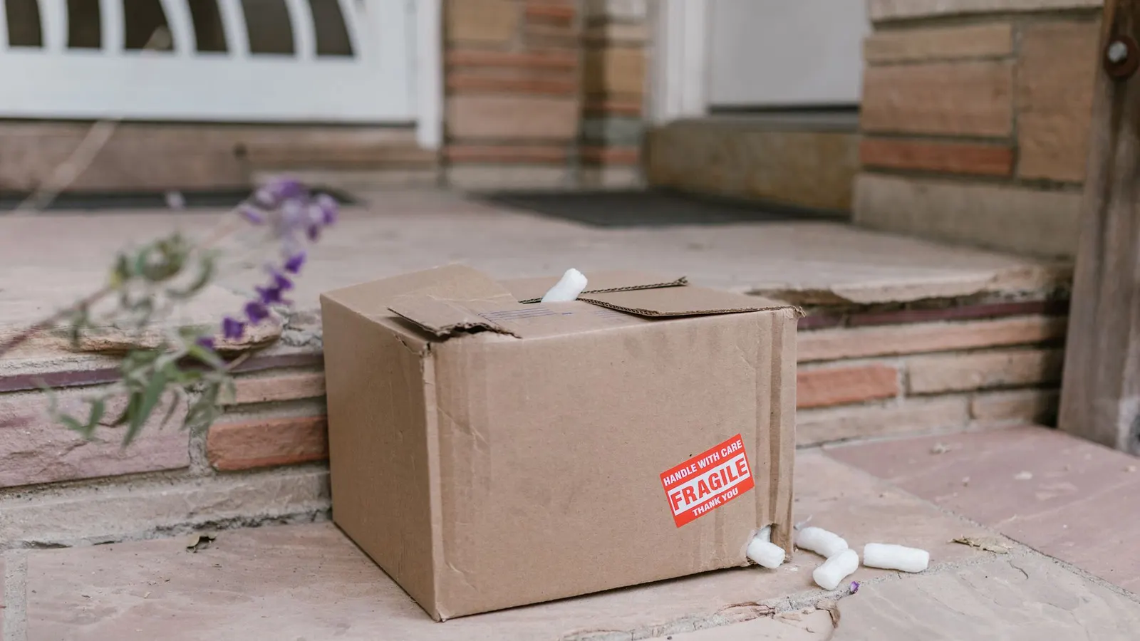 A split cardboard box with a Fragile label and packing peanuts spilling out onto a doorstep