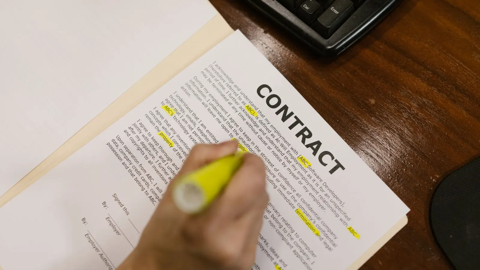 A hand highlighting clauses in yellow on a printed contract, with the word CONTRACT visible at the top of the page