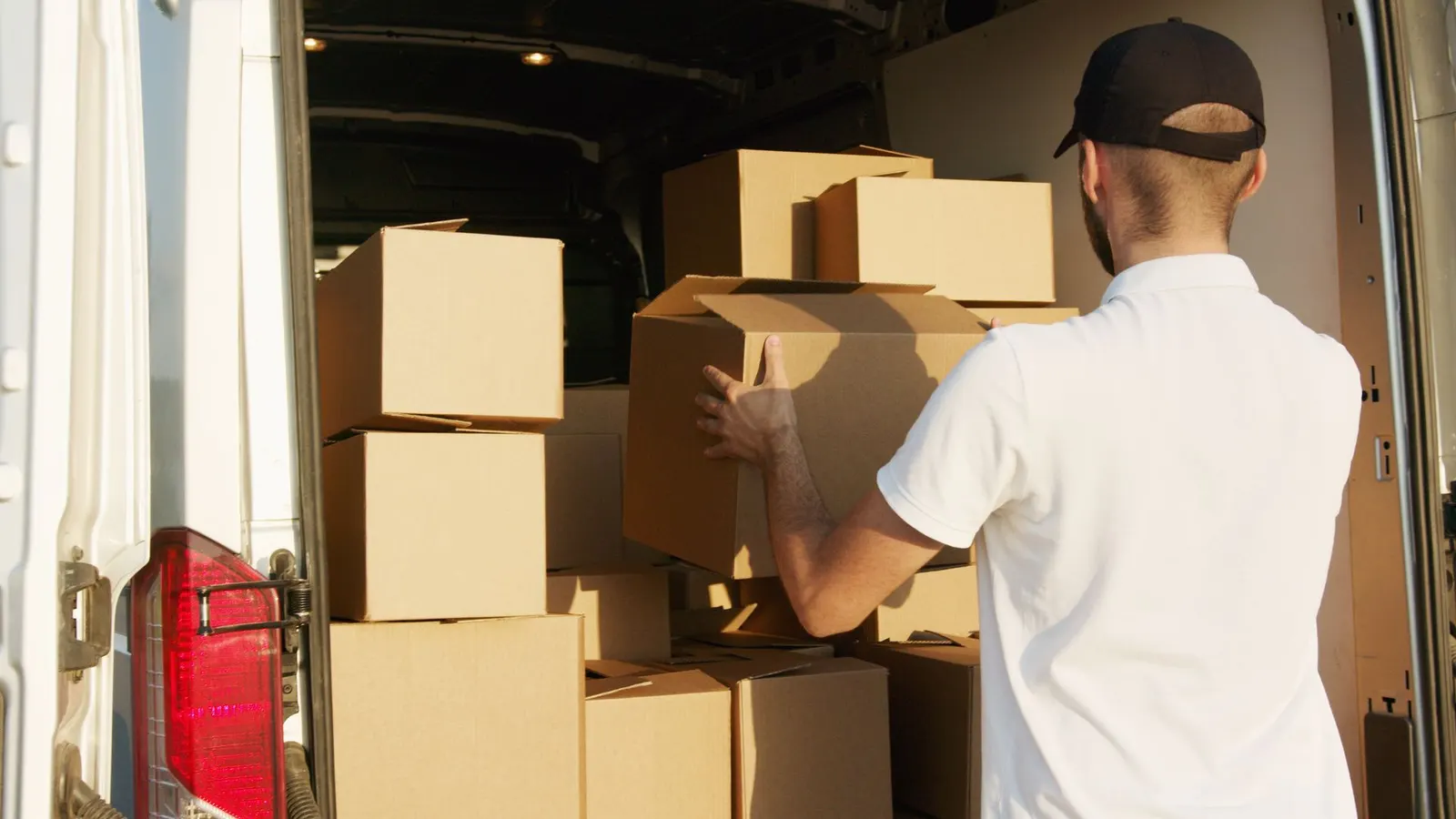 A courier stacking cardboard boxes into the back of a van