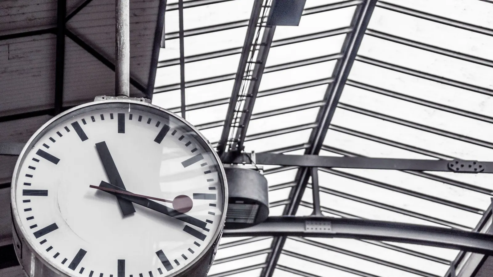 A station clock hanging under a glass roof
