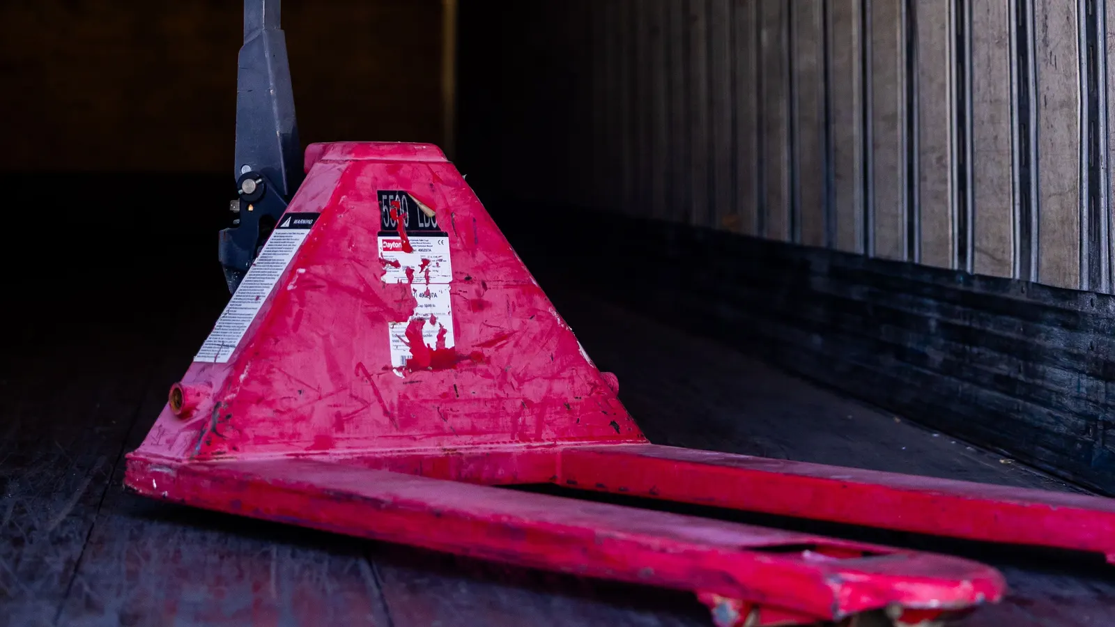 A red pallet jack standing inside an empty truck trailer