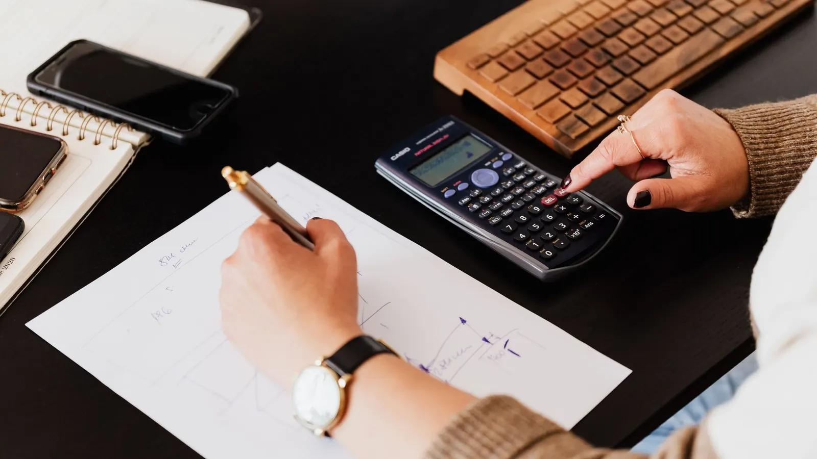Hands working through figures with a calculator and paperwork at a desk