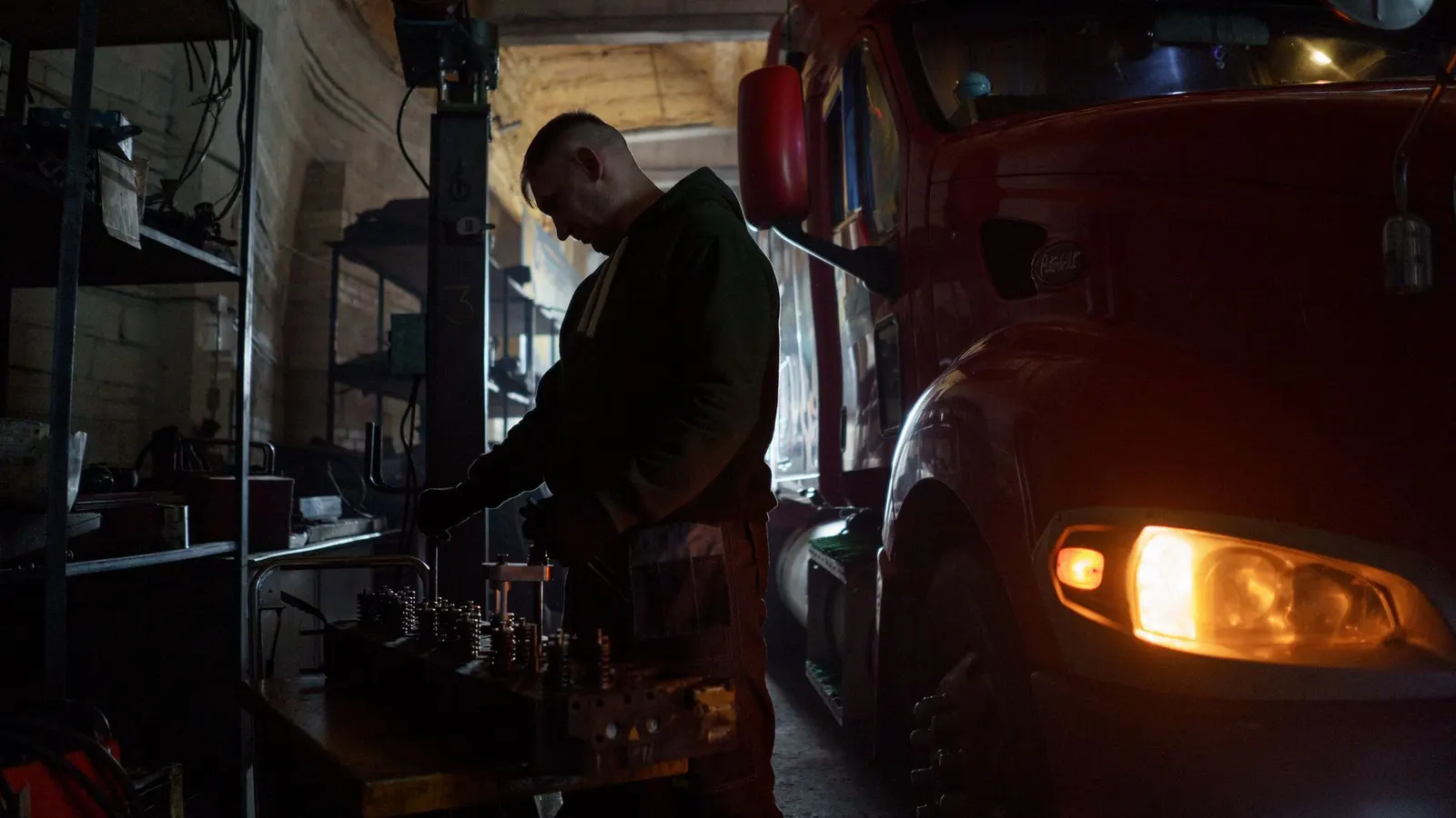A mechanic working on an engine component beside a truck in a workshop
