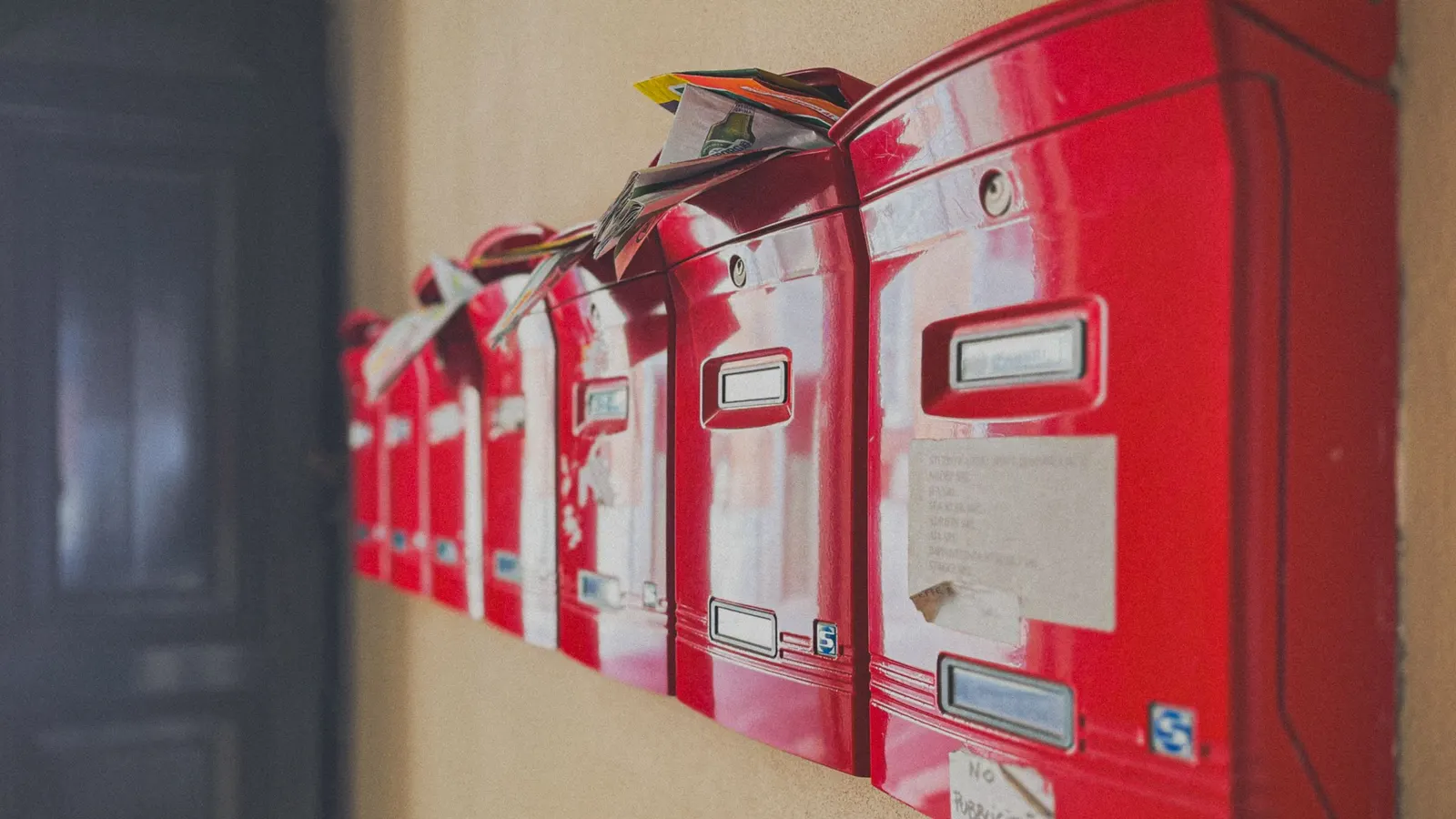 Row of red apartment letterboxes with unread post spilling out of the tops, and a handwritten note taped to the nearest one