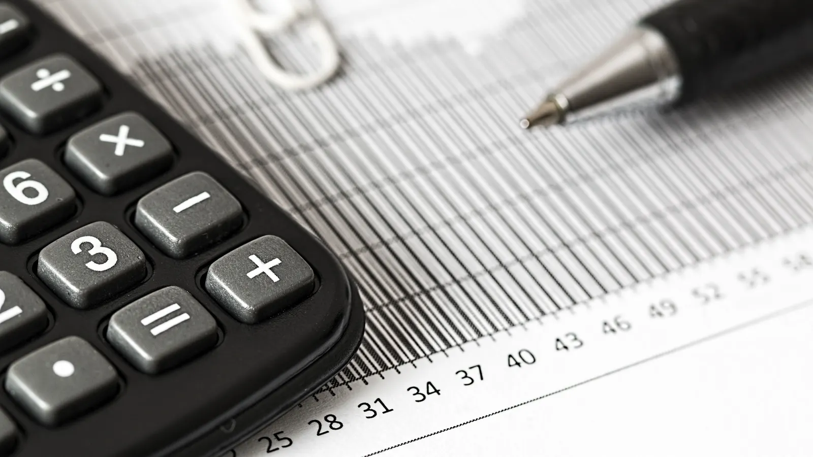 A calculator and pen resting on a printed bar chart with a ruled numeric scale