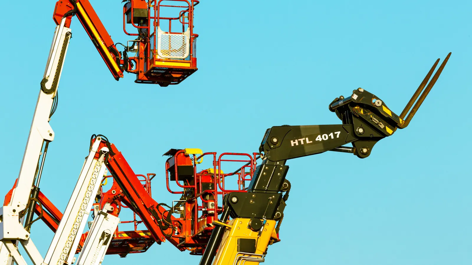 Raised aerial work platforms and a telehandler against a clear blue sky