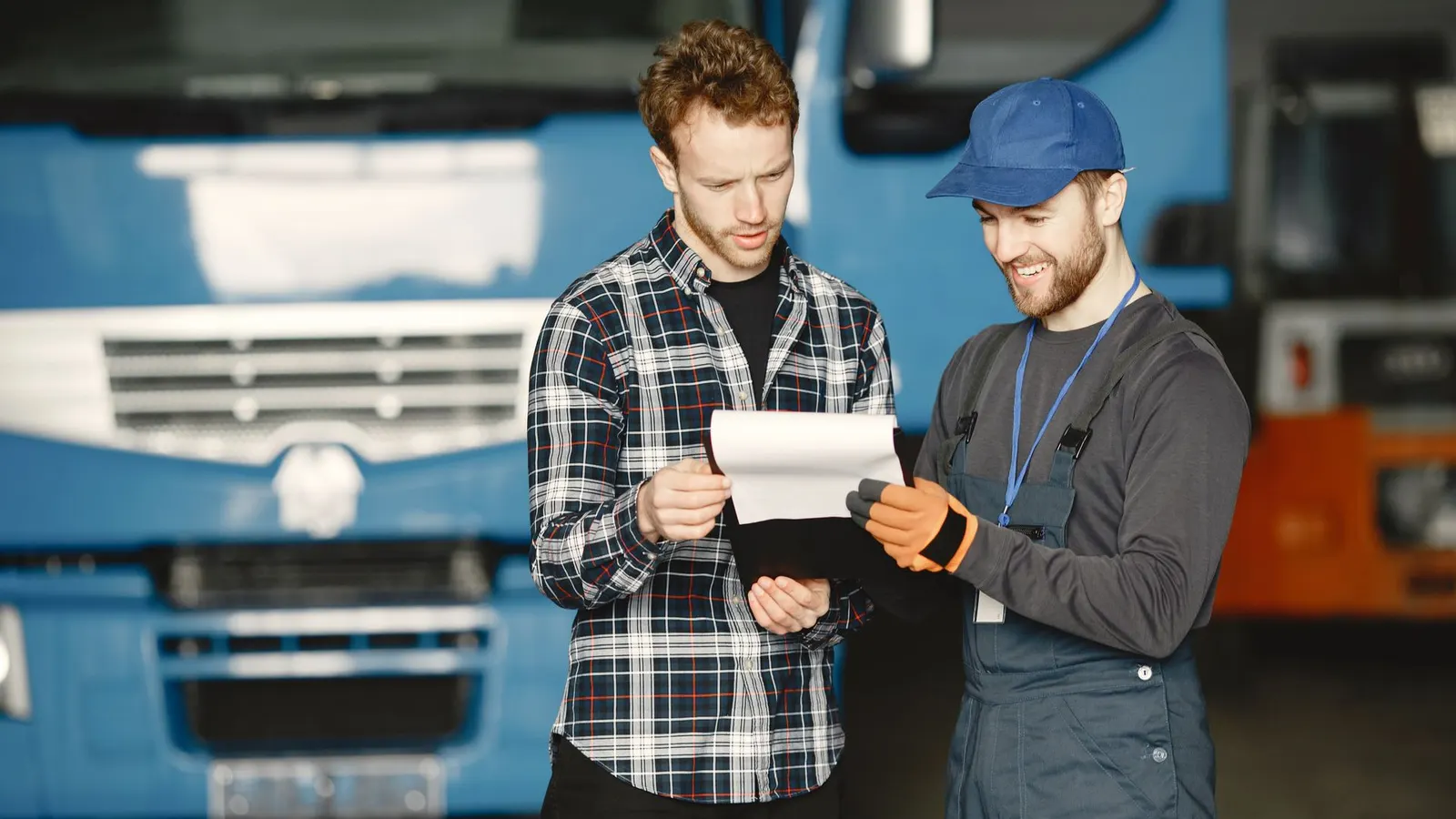 Two men in a workshop reading a document in front of a blue truck