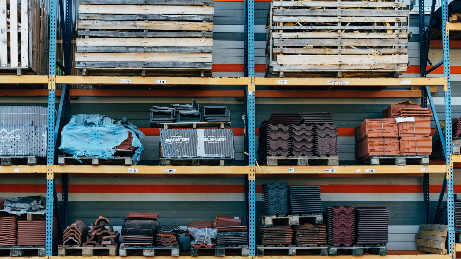 Rayonnages d’entrepôt chargés de tuiles et de matériaux de construction sur palettes, dont une palette emballée dans un film bleu