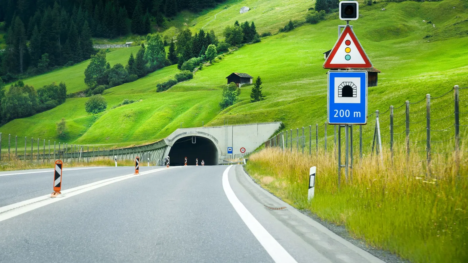 A European road approaching a tunnel entrance, with tunnel warning signs