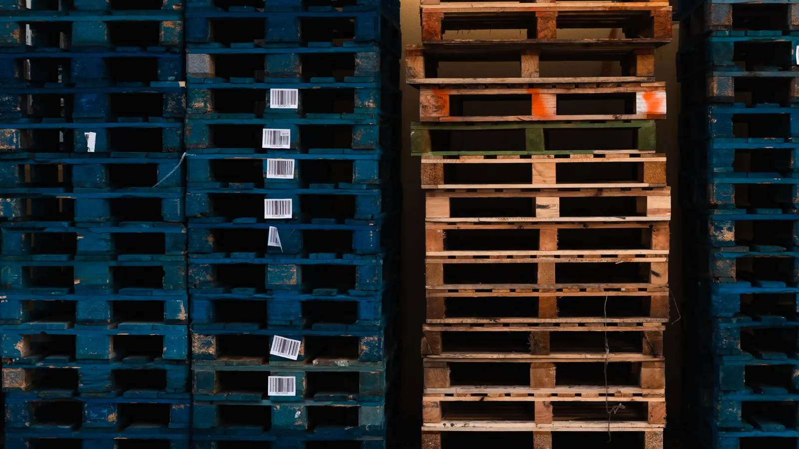 Stacks of blue and natural wooden pallets, several bearing white barcode labels