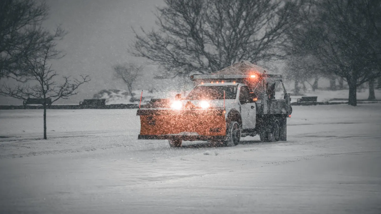 A plough truck working in falling snow with its headlights on
